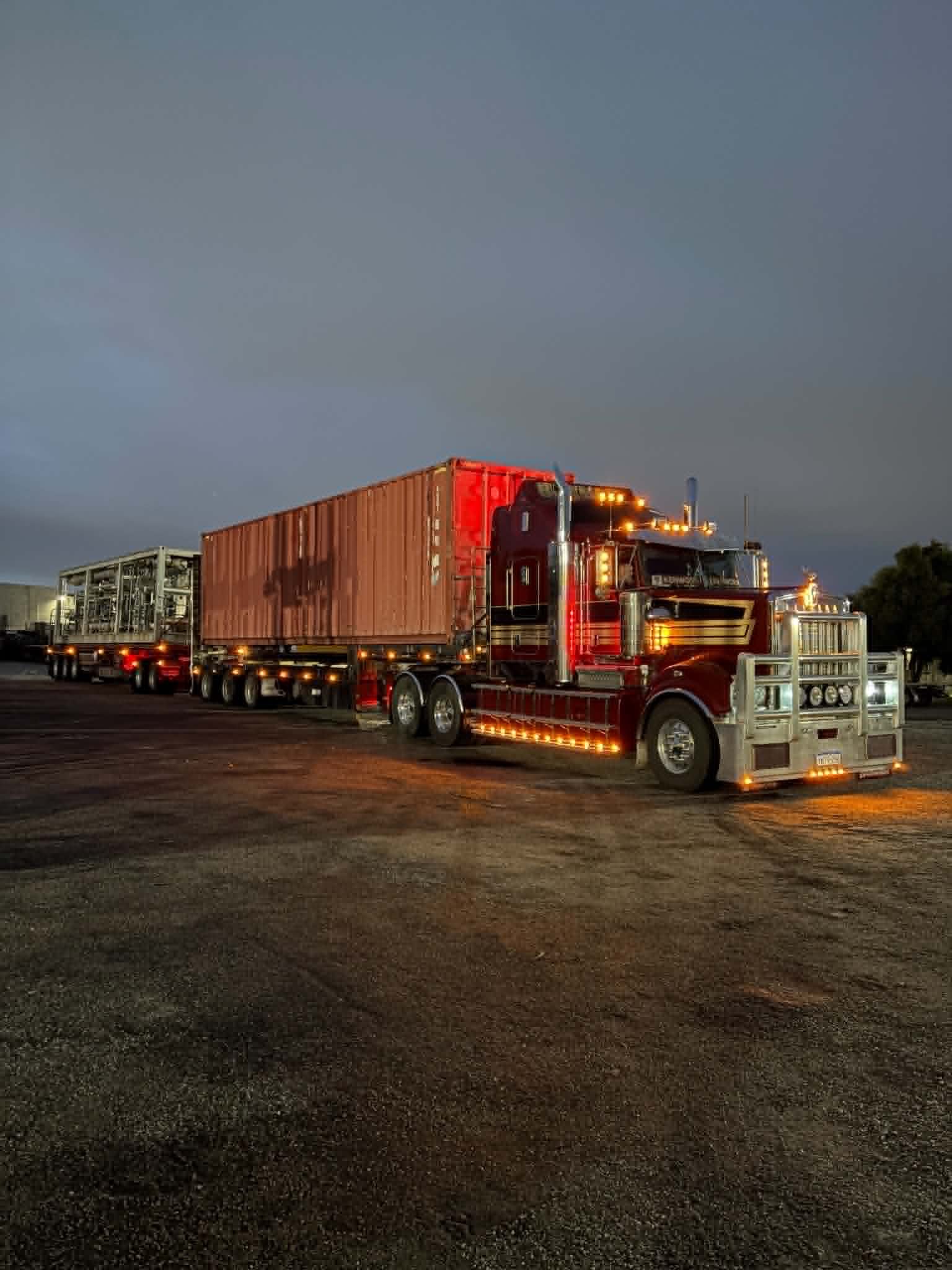 G&S Hannah Transport Kenworth road train loaded with a shipping container and a plant module, lit up at dusk before heading for North Queensland.
