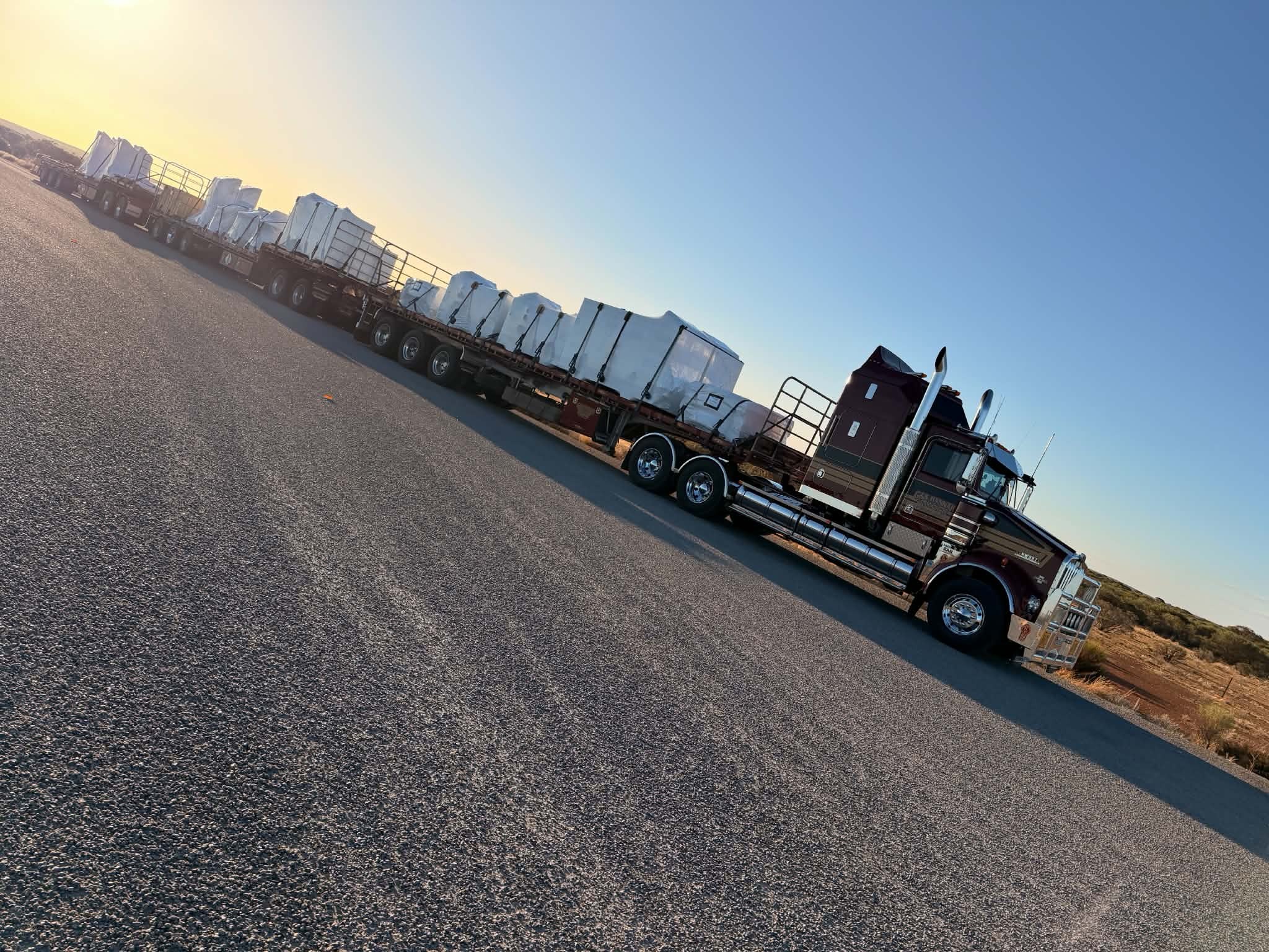 G&S Hannah Transport Kenworth triple road train loaded with wrapped freight on a red dirt roadside, heading for Townsville.