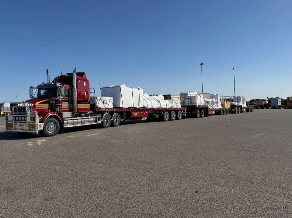 Red G&S Hannah Transport Kenworth pulling three flat-top trailers of wrapped freight, ready to leave for Townsville.
